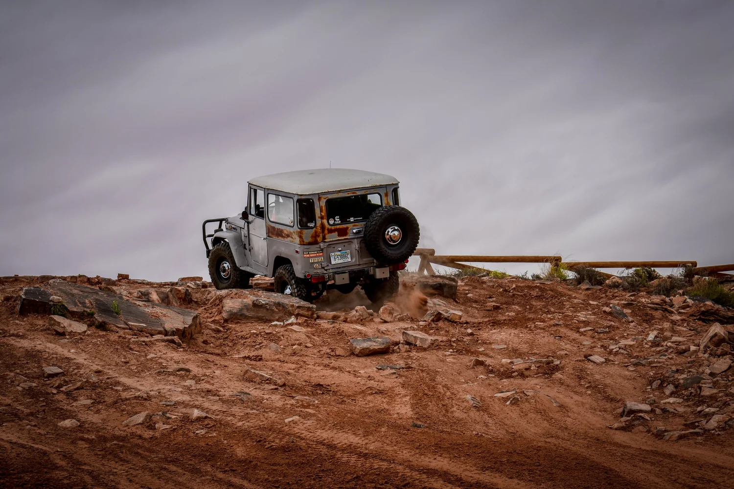 Gray Toyota FJ40 Land Cruiser climbing a rock ledge under a cloudy sky on the 3D Trail at Cruise Moab