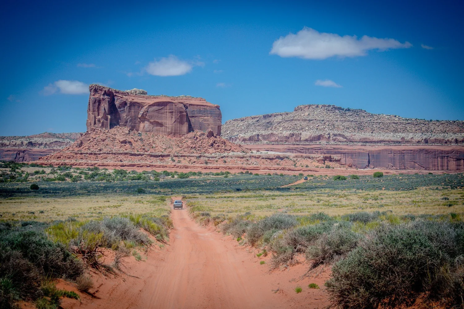 Red sand two-track through sagebrush toward a large butte under a blue sky on the Seven Mile Rim trail near Moab, Utah