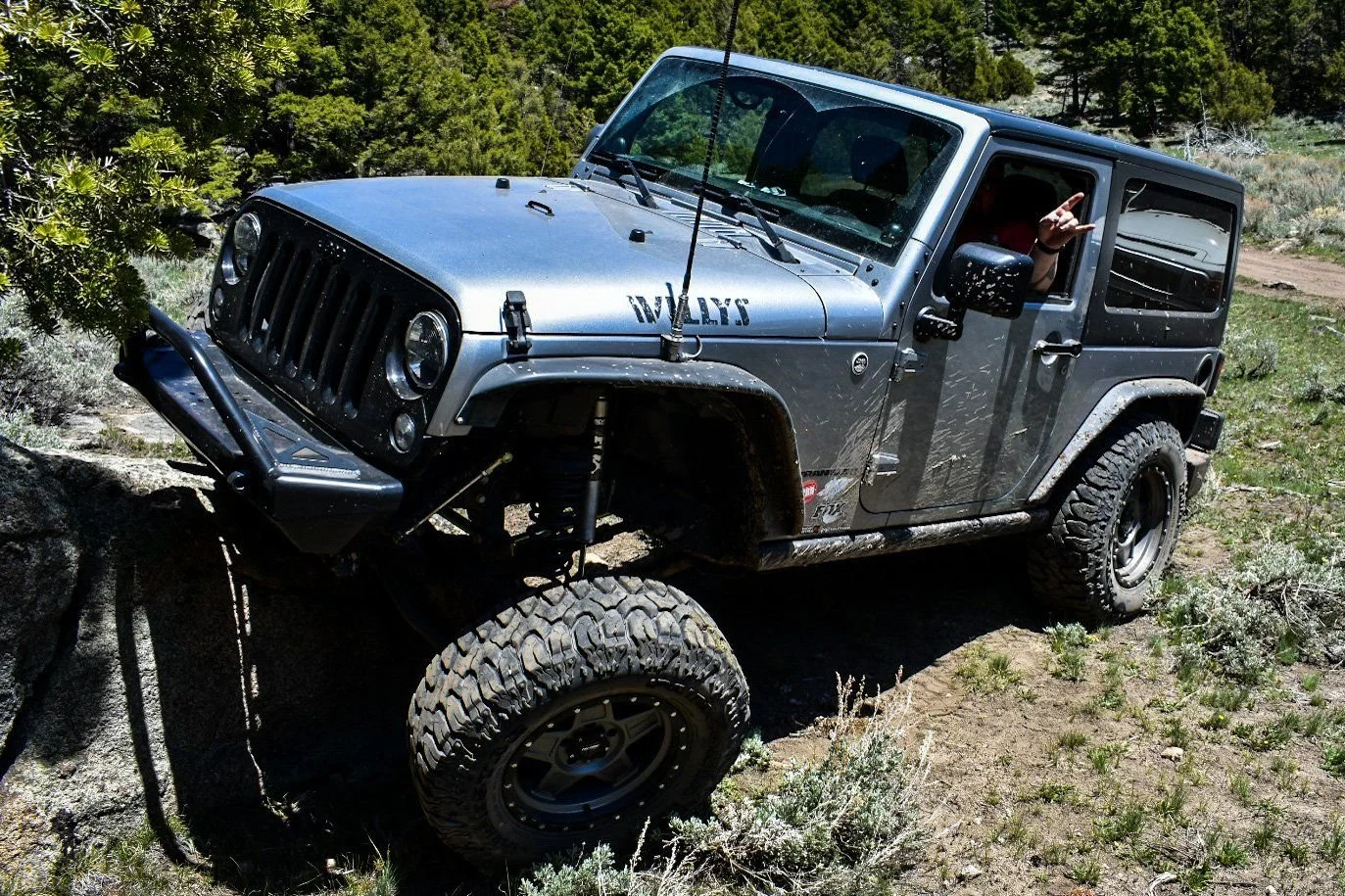 Gray Jeep Wrangler with a Willys decal flexing over a rock on the Ringing Rocks trail near Pipestone, Montana