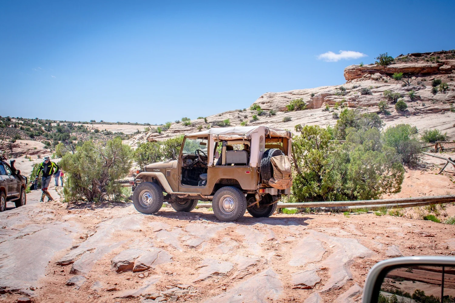 Olive tan soft-top Toyota FJ40 on slickrock beside junipers on the Seven Mile Rim trail near Moab, Utah