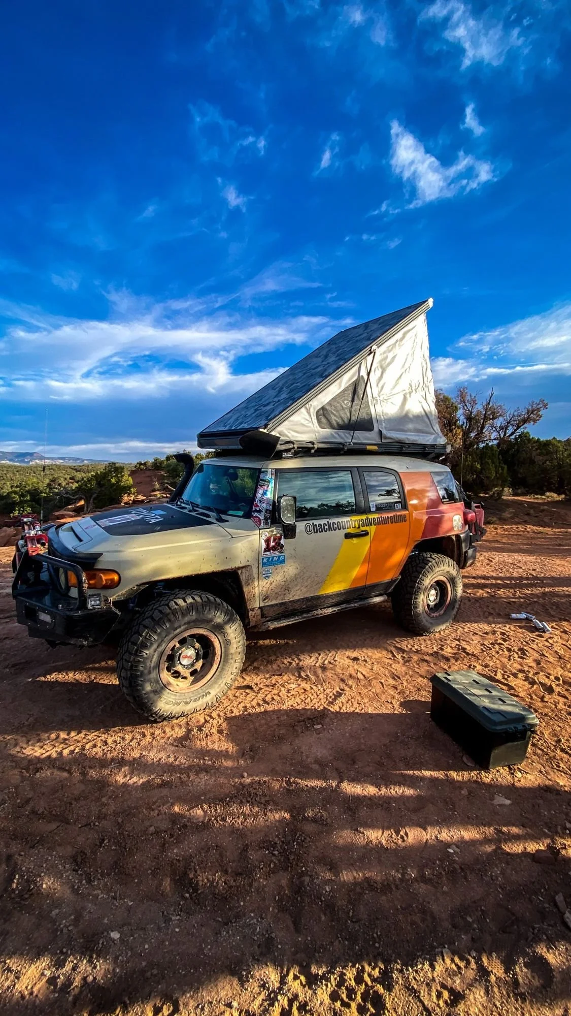 Striped FJ Cruiser with a pop-up rooftop tent on red slickrock under a blue sky on a spring road trip through Utah