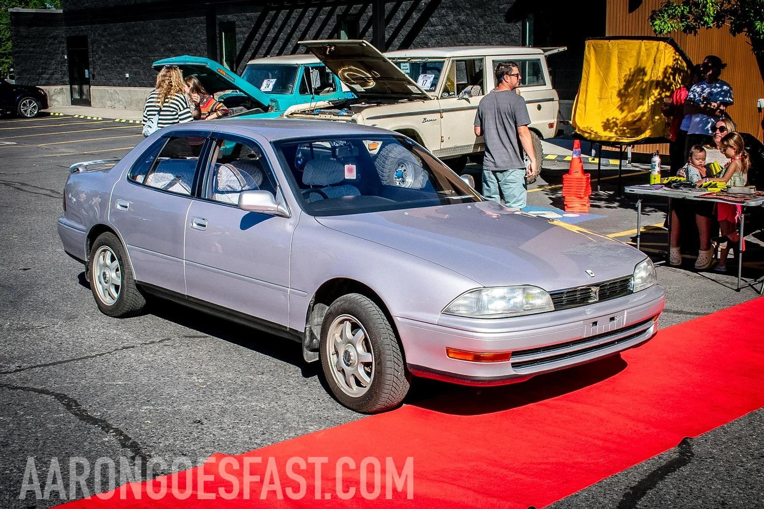 Lavender silver 1990s Toyota Camry sedan parked on a red carpet at the Roly-Poly Daily Driver Show in Bozeman