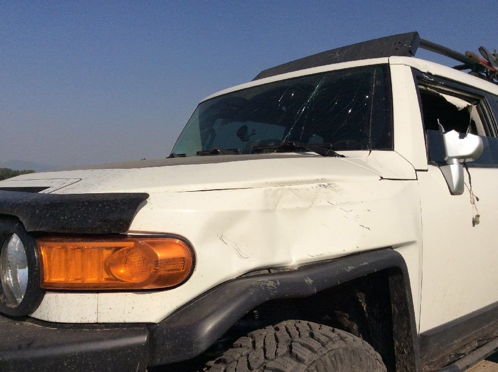 Close view of a dented hood and fender on a white FJ Cruiser on a rocky forest trail in Montana