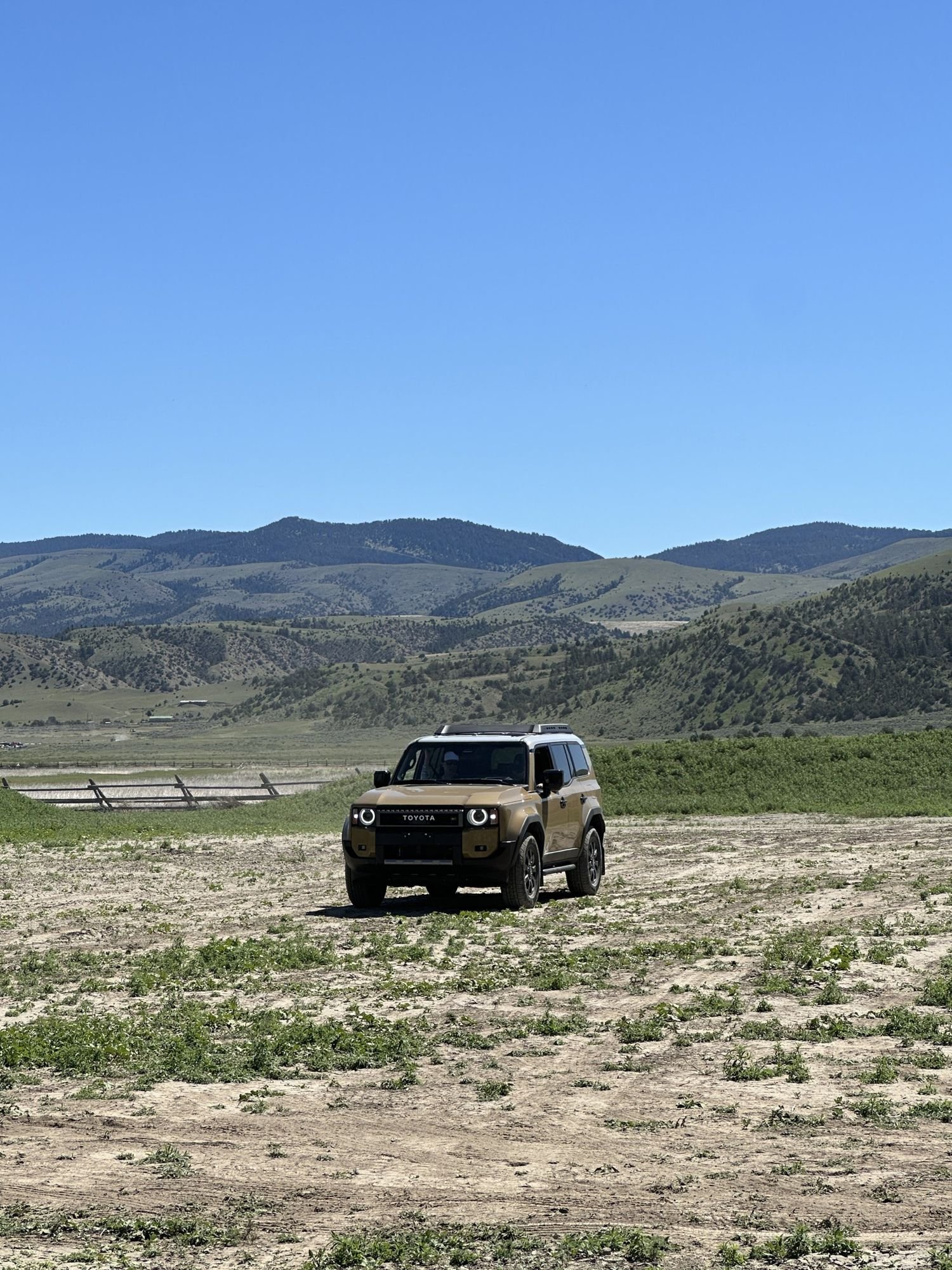 Tan Land Cruiser 250 on a dirt course below green hills at XOverland Ranch near Bozeman, Montana