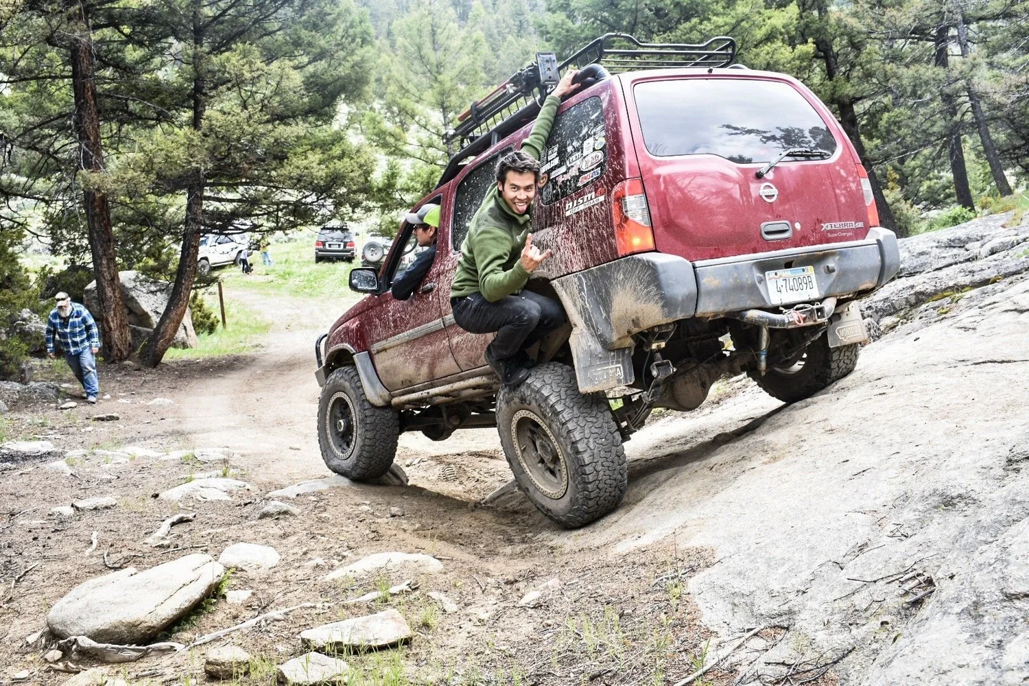Red Nissan Xterra flexed hard on a granite slab with a passenger leaning out the window on the Ringing Rocks trail near Pipestone, Montana