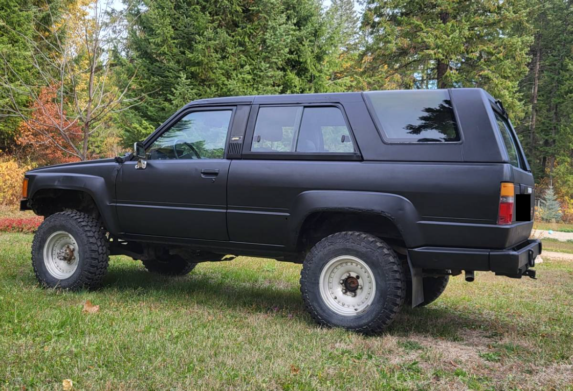 Side view of a flat black 1985 Toyota 4Runner on mud tires