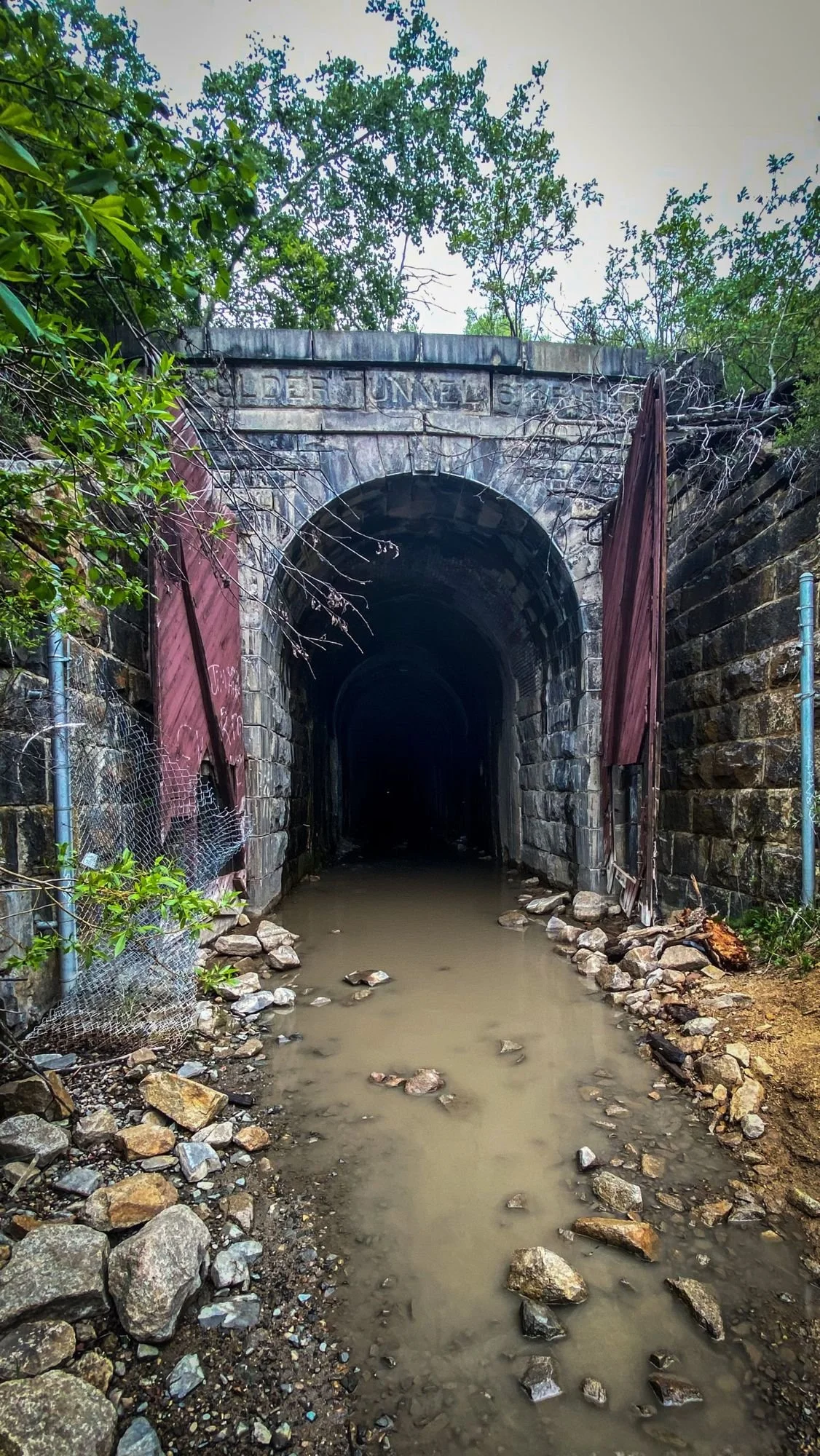Arched stone portal of the Wickes railroad tunnel with old red wooden doors hanging open and standing water on the floor at the Wickes railroad tunnel near Jefferson City, Montana