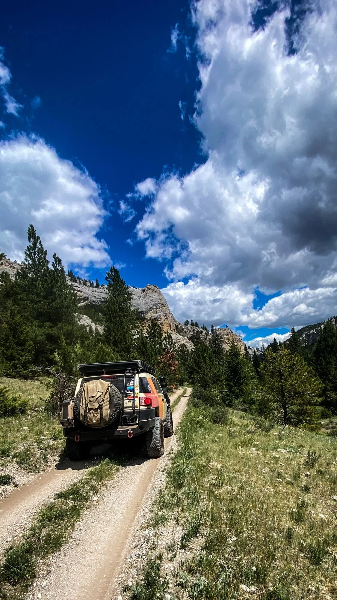 Striped FJ Cruiser driving a two-track into a canyon under dramatic clouds on the Middle Fork Judith River road in the Little Belt Mountains, Montana