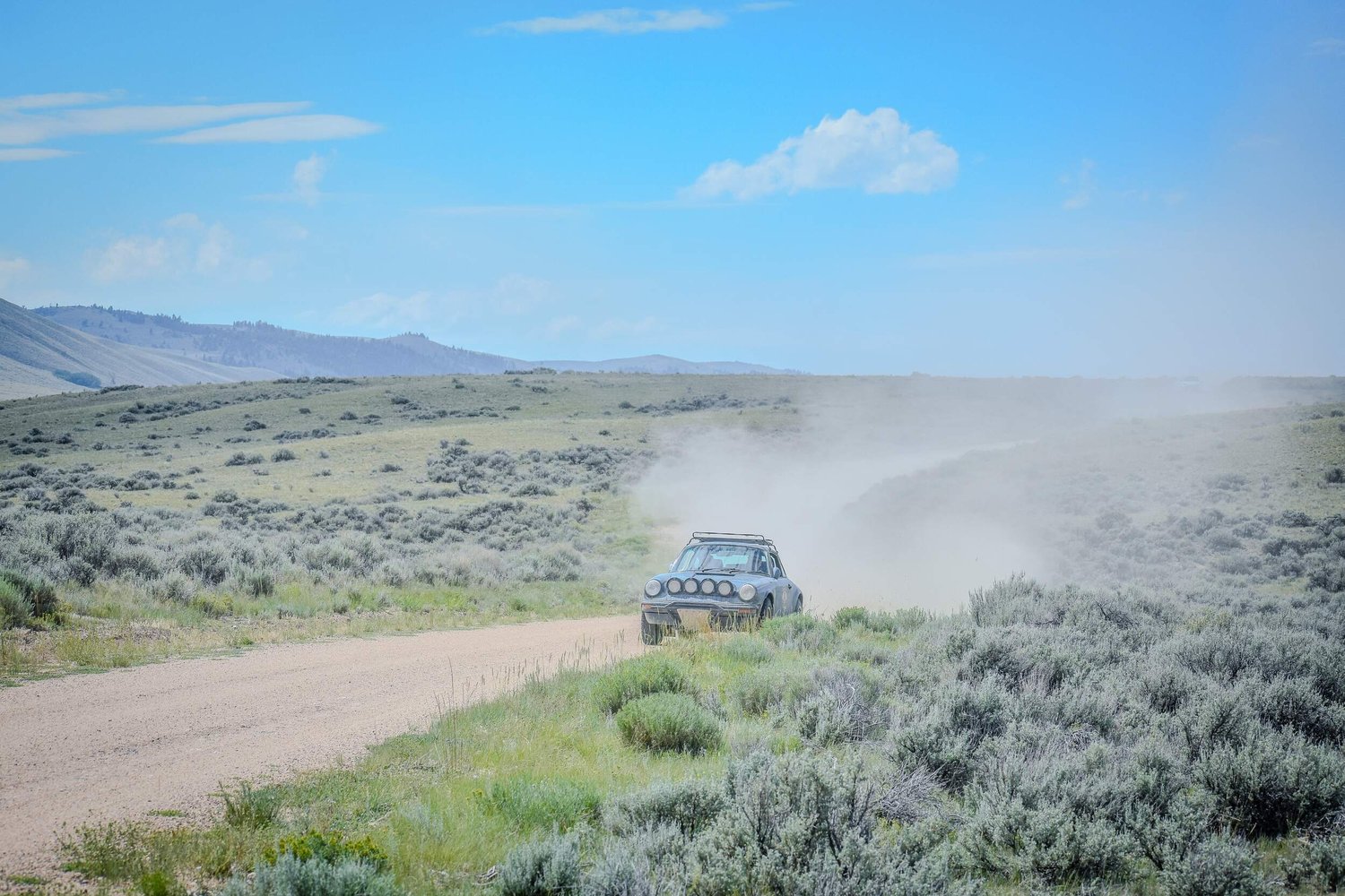 Rally vehicle and rolling dust cloud crossing Montana sagebrush country