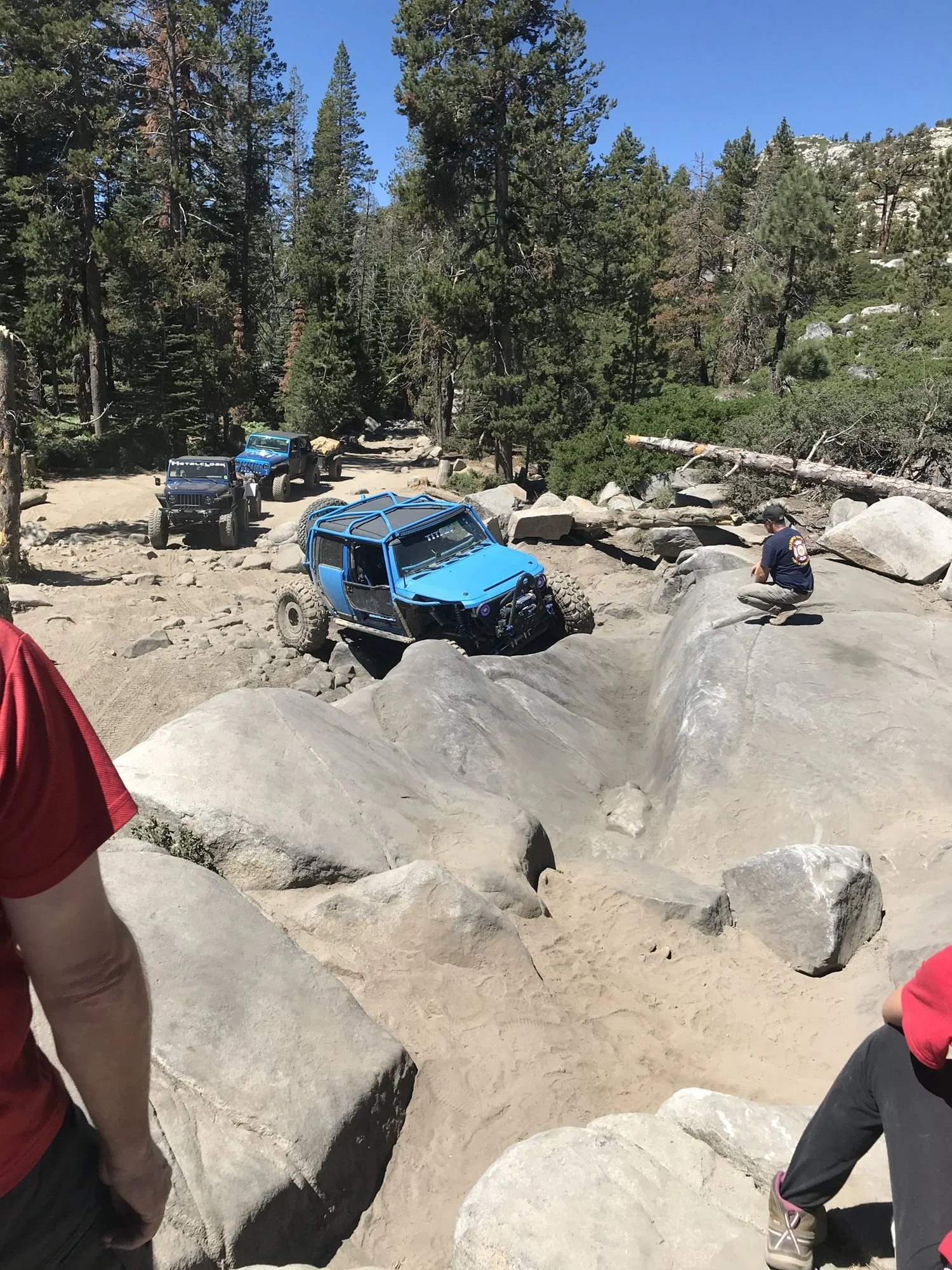 Blue Jeep in a granite bowl full of smooth boulders with spectators in the foreground on the Rubicon Trail in California during Rubithon 2022