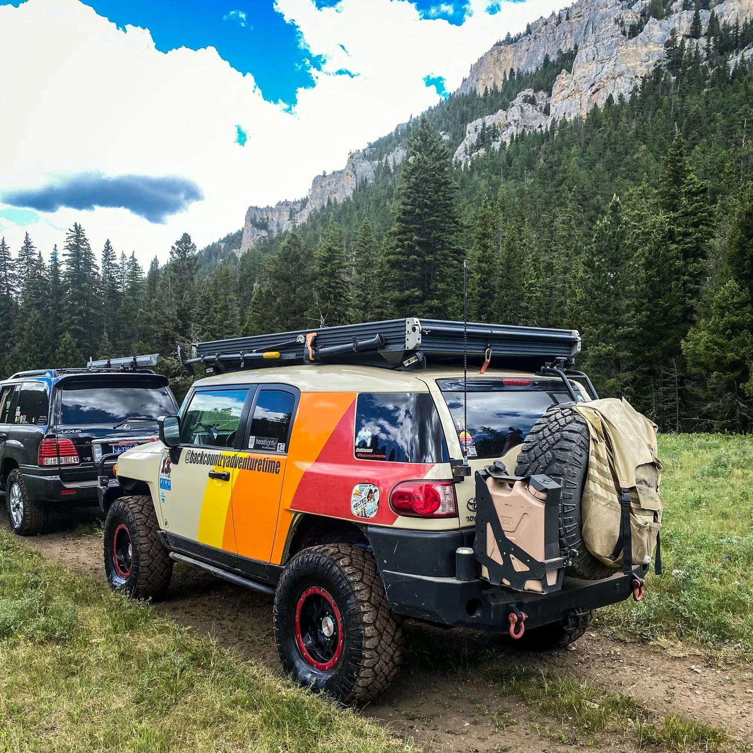 Toyota FJ Cruiser with orange and red stripes and a rooftop tent parked below limestone cliffs on the Middle Fork Judith River road in the Little Belt Mountains, Montana