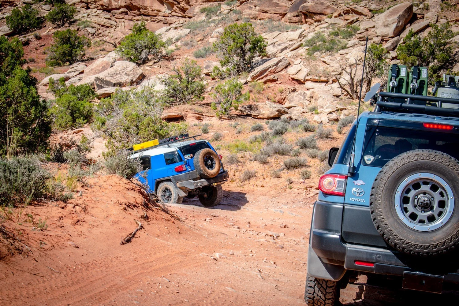 Bright blue Toyota FJ Cruiser leaning on an off-camber bank with another FJ Cruiser in the foreground on the Seven Mile Rim trail near Moab, Utah