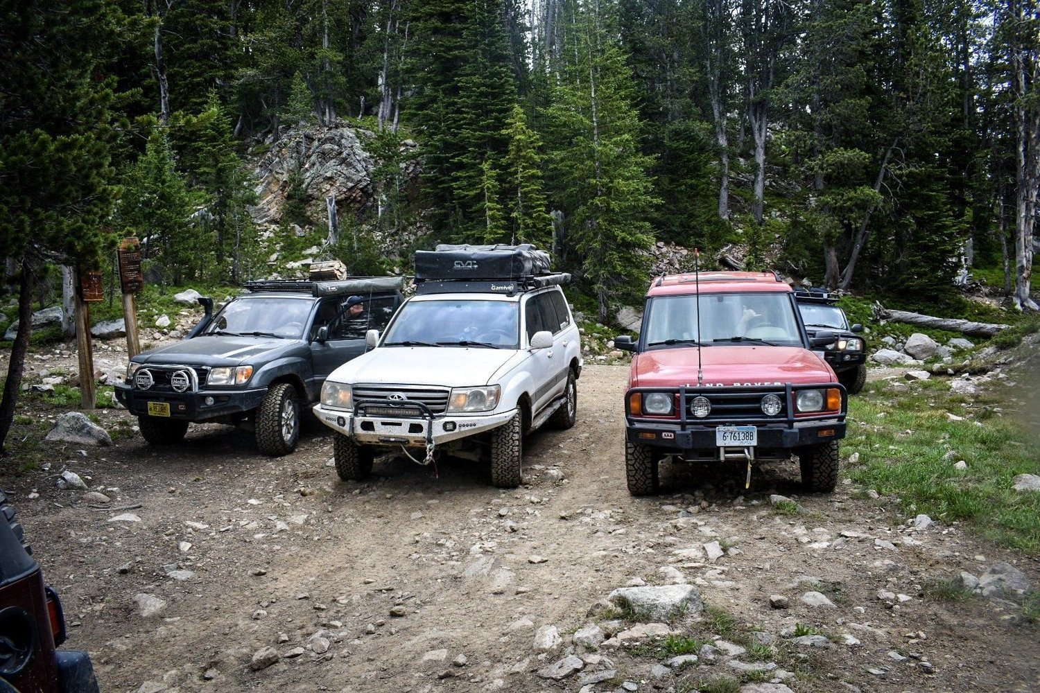 Dark 4Runner, white Land Cruiser 100 Series and red Land Rover Discovery lined up at a rocky trailhead in the trees near Cooke City, Montana