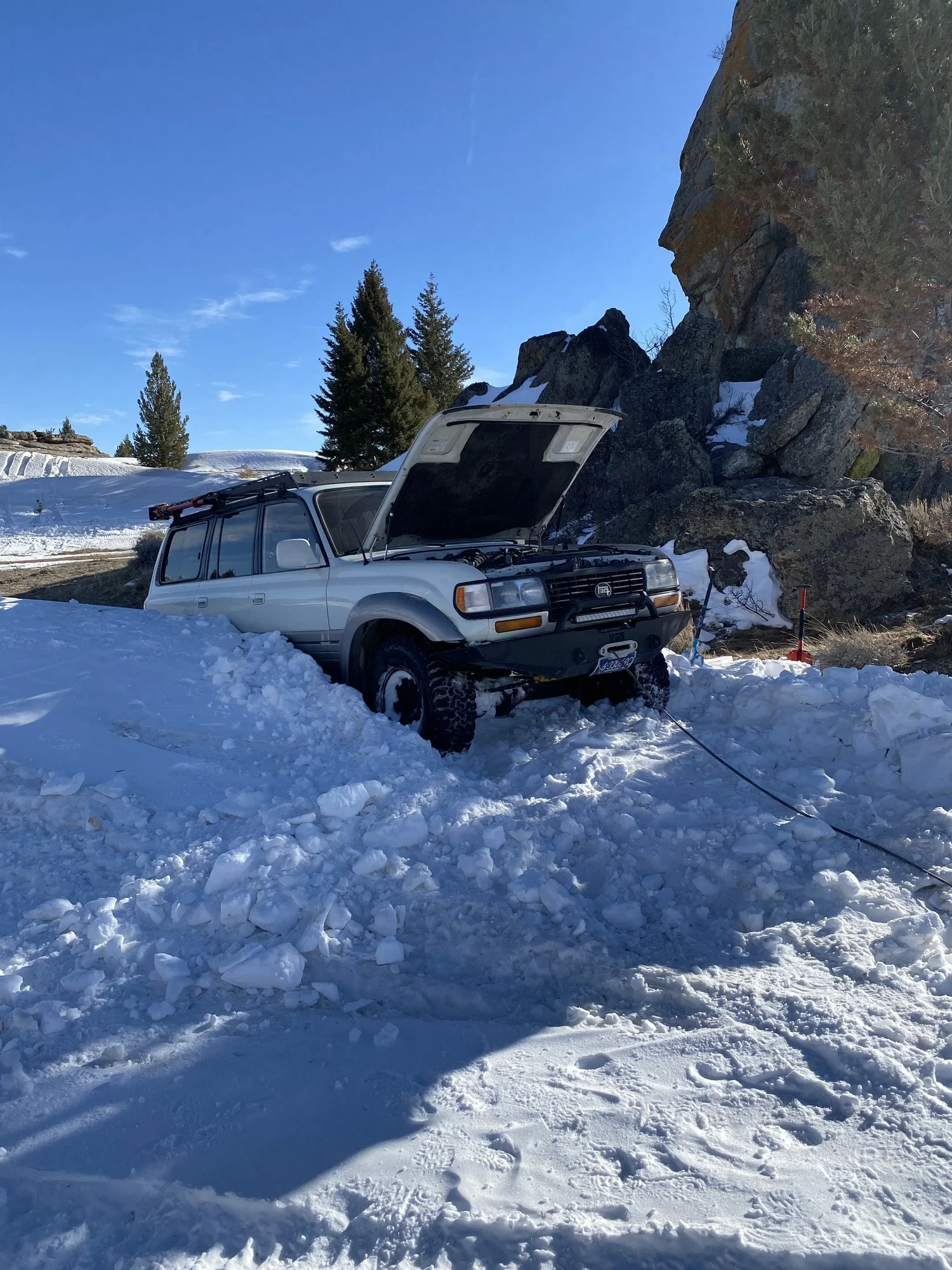 White 80 Series Land Cruiser dug out in deep snow with its winch line run from the front bumper during a February snow wheeling run in Montana