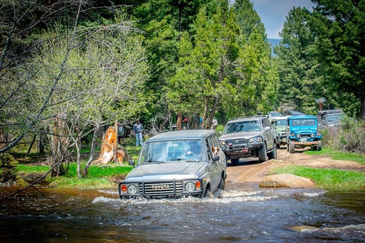 An 80 Series Land Cruiser pushing through a creek crossing with more Land Cruisers lined up behind it.