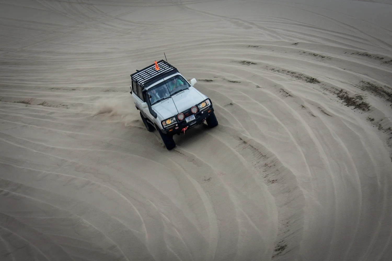 White Toyota Land Cruiser 80 Series with a snorkel and bull bar carving through rippled sand at the St. Anthony Sand Dunes in Idaho