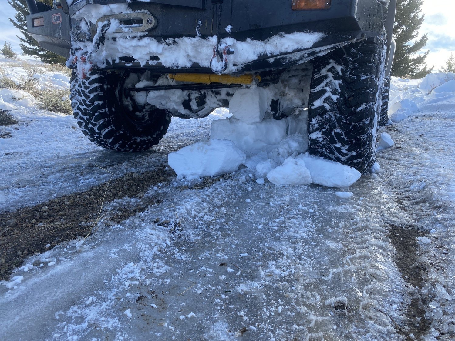 Chunks of packed snow knocked loose under the rear axle of a truck on an icy trail during a February snow wheeling run in Montana