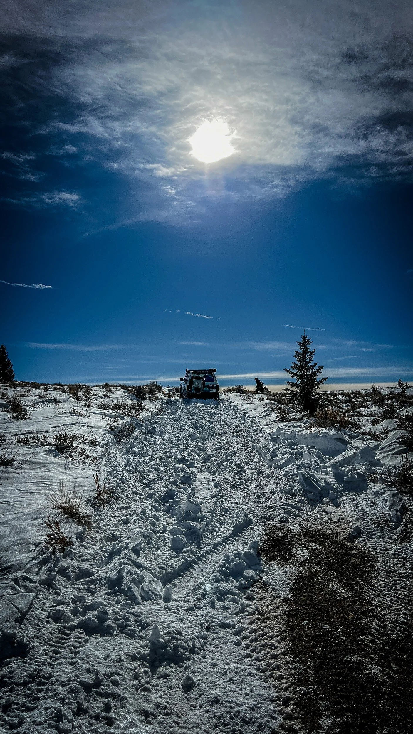A trench of broken, churned snow through sagebrush leading to a distant truck during a February snow wheeling run in Montana