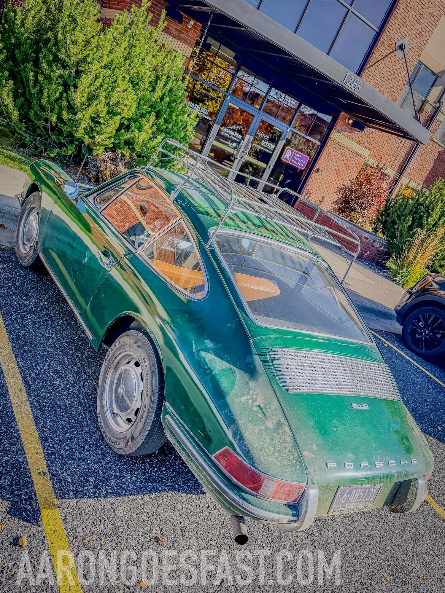 Rear three-quarter view of the dusty green Porsche 912 showing the 912 decklid badge, PORSCHE script, chalky paint and roof rack