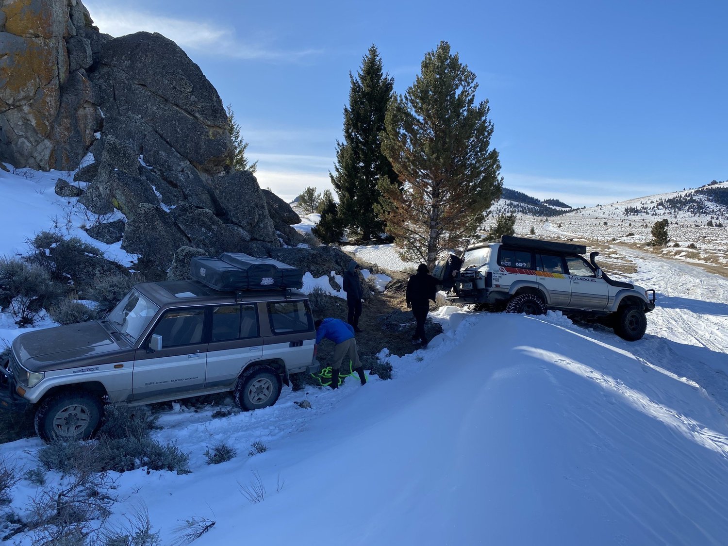 Green and yellow kinetic recovery rope laid out between a Land Cruiser with a rooftop tent and a striped Lexus LX450 in deep snow during a February snow wheeling run in Montana