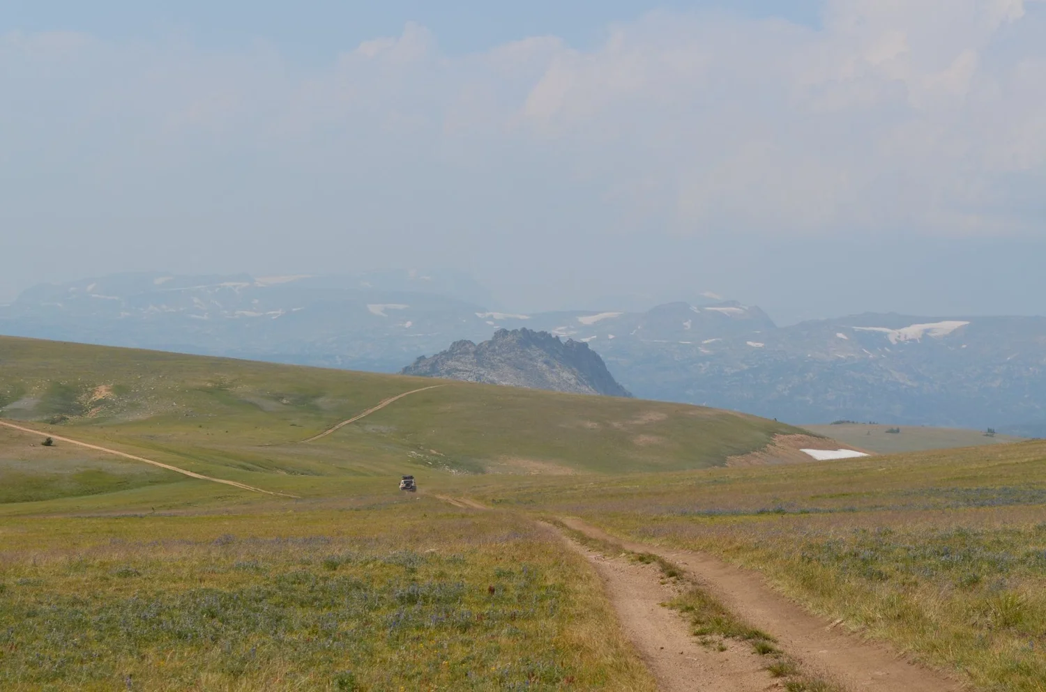 Dirt two-track crossing a wide plateau toward a distant rock outcrop and hazy mountains on the Morrison Jeep Trail in Clarks Fork Canyon near Cody, Wyoming
