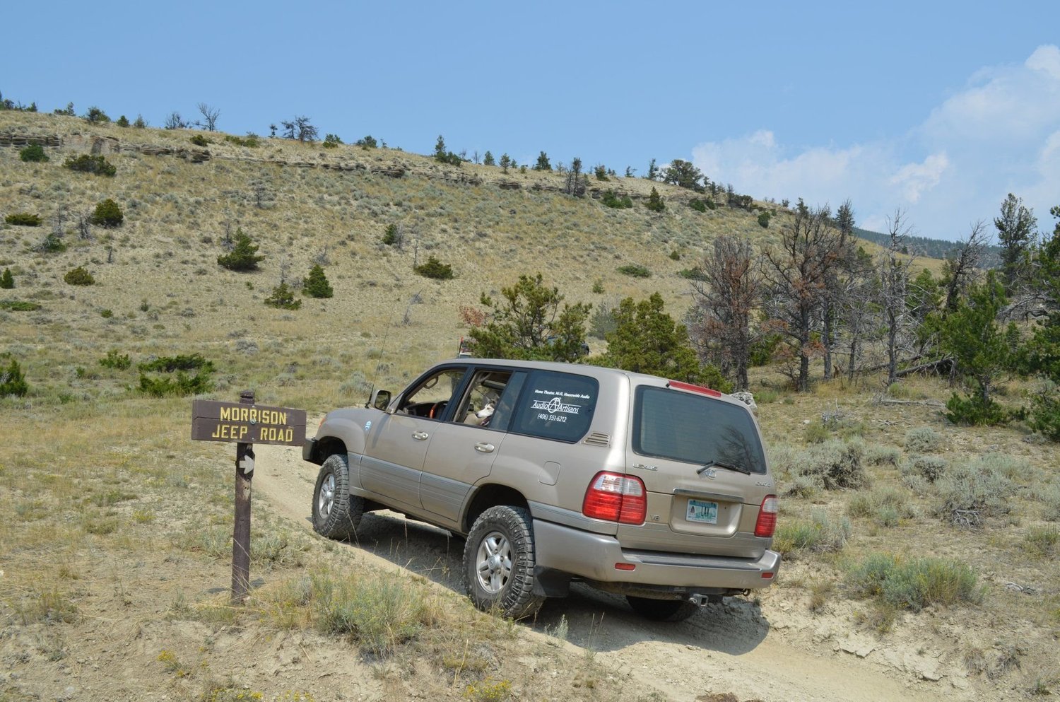 Champagne Toyota Land Cruiser passing a wooden Morrison Jeep Road sign on a sagebrush hillside on the Morrison Jeep Trail in Clarks Fork Canyon near Cody, Wyoming