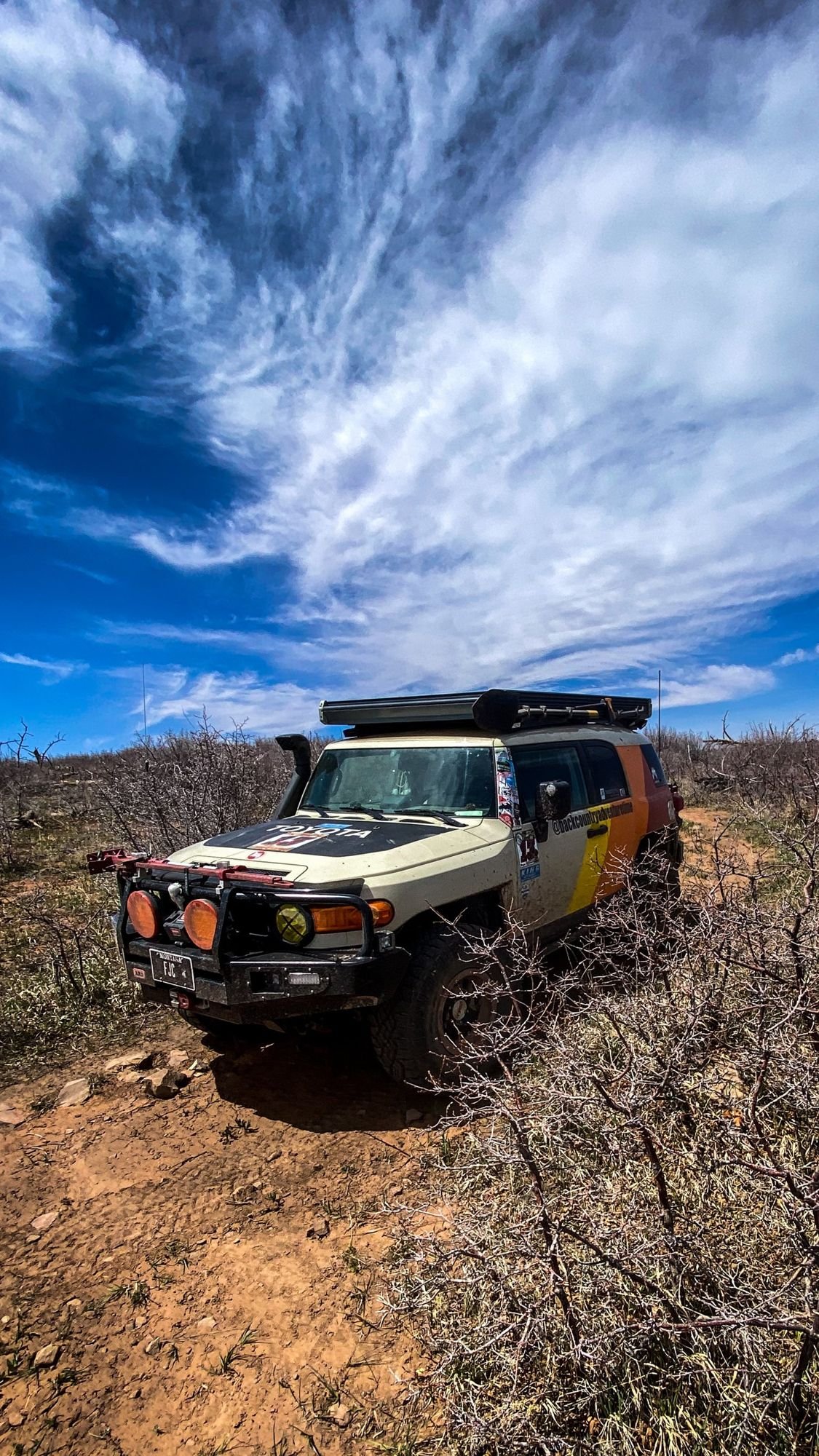 Striped FJ Cruiser on a sandy trail under swirling cirrus clouds on a spring road trip through Utah