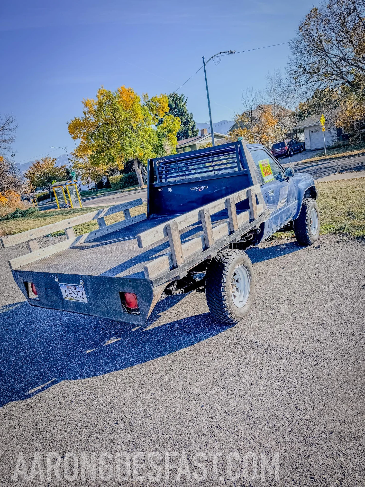 Rear three-quarter view of the blue 1987 Toyota Pickup showing its steel flatbed, wooden stake rails, headache rack and all-terrain tires