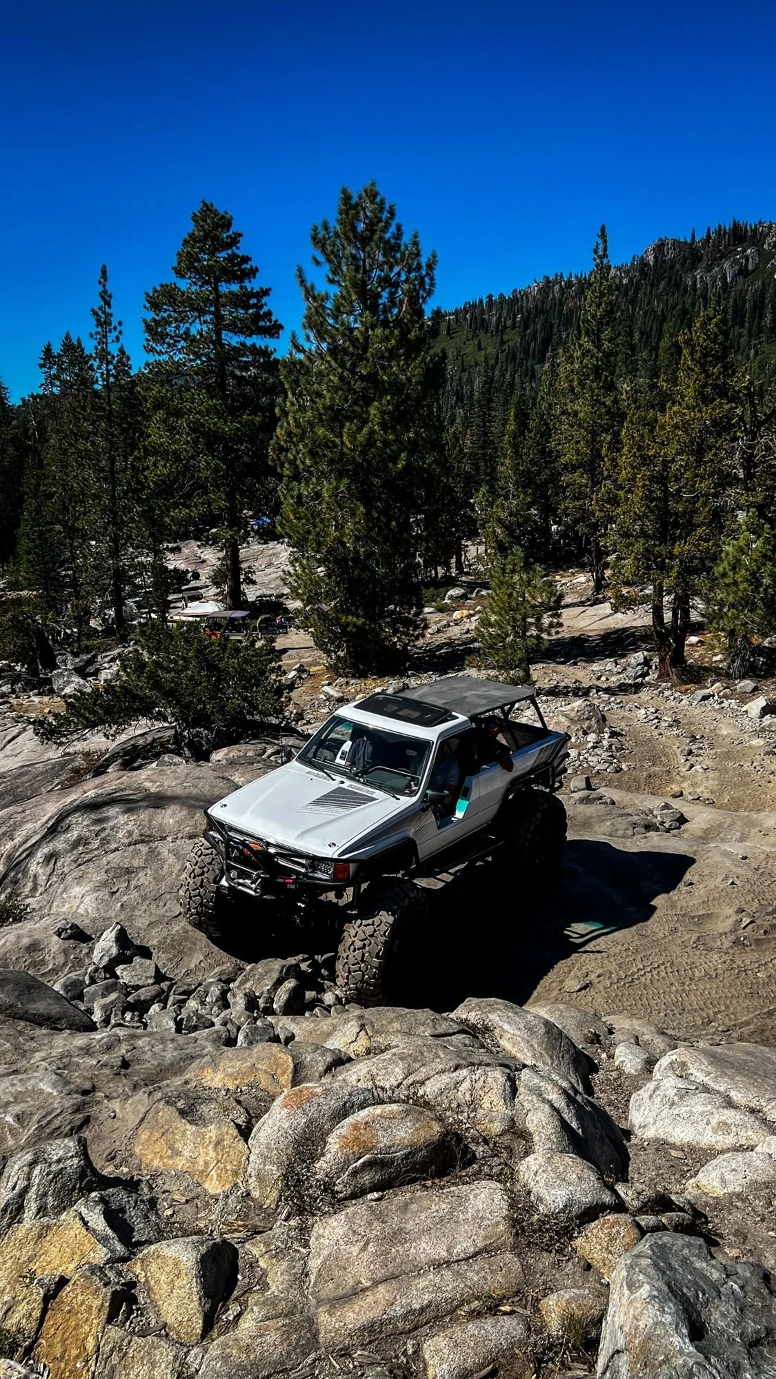 White off-road truck climbing granite steps below a pine-covered ridge on the Rubicon Trail in California during Rubithon 2022