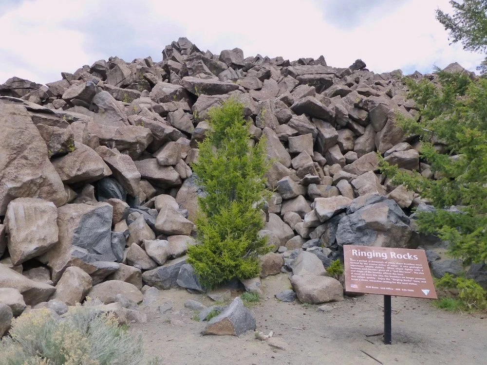 Large pile of dark angular boulders with a small pine tree and the Ringing Rocks interpretive sign near Pipestone, Montana