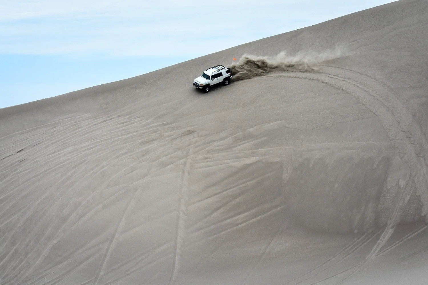 White Toyota FJ Cruiser crossing a steep dune face with a long plume of sand behind it at the St. Anthony Sand Dunes in Idaho
