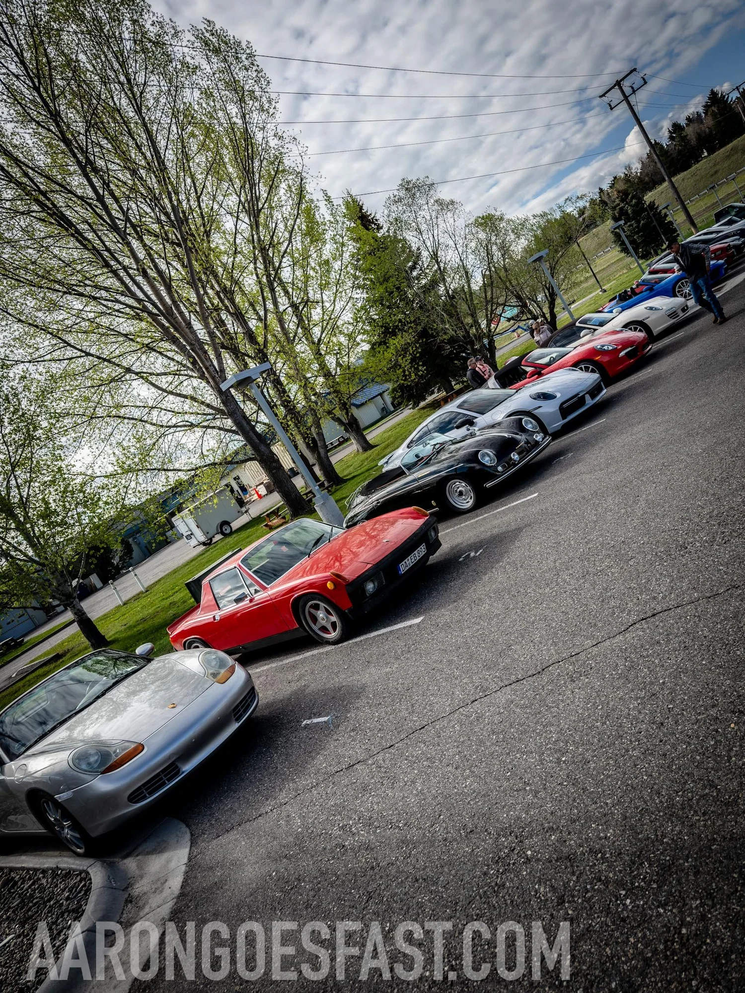 A line of Porsches, including a Boxster and a red 914, parked along the curb at Gallatin Subaru