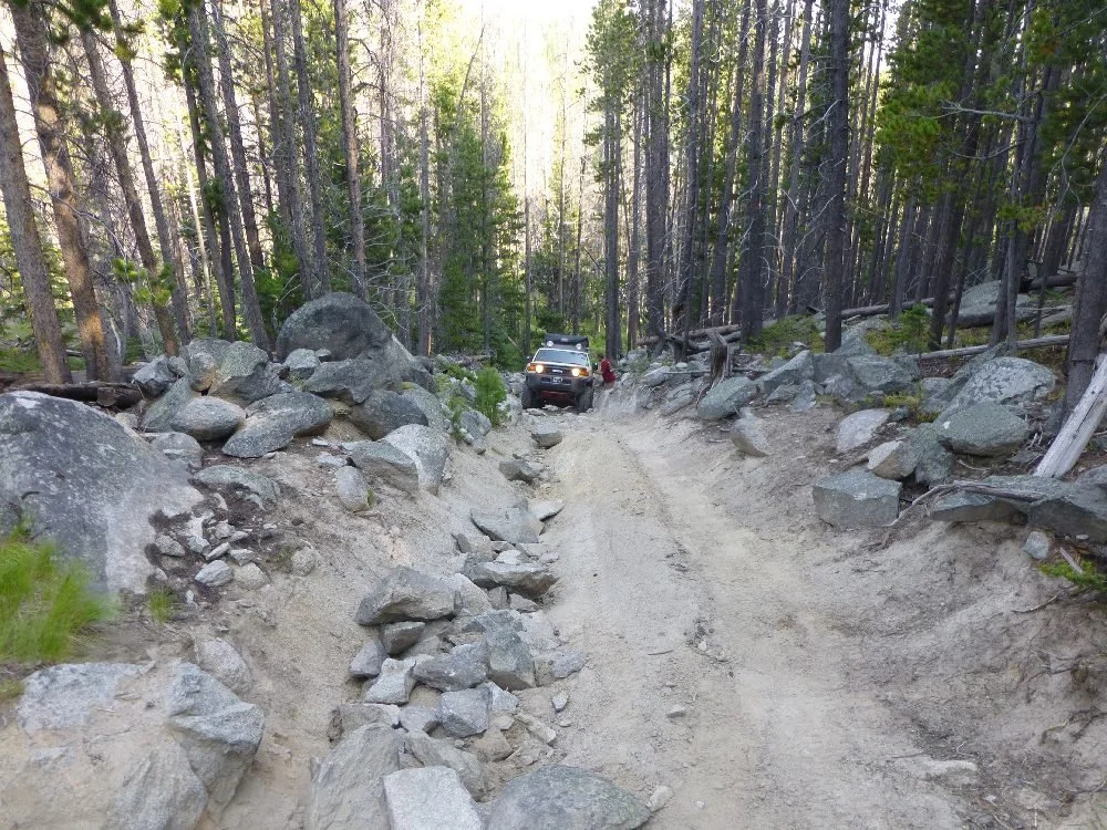 Long view down a sandy track lined with boulders, with rigs far ahead
