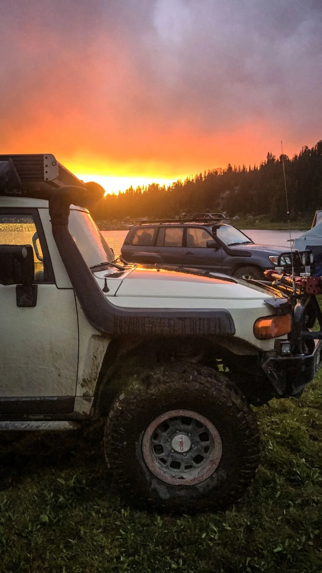 Silhouetted trucks with a snorkel and roof rack under a fiery orange sunset sky near Cooke City, Montana