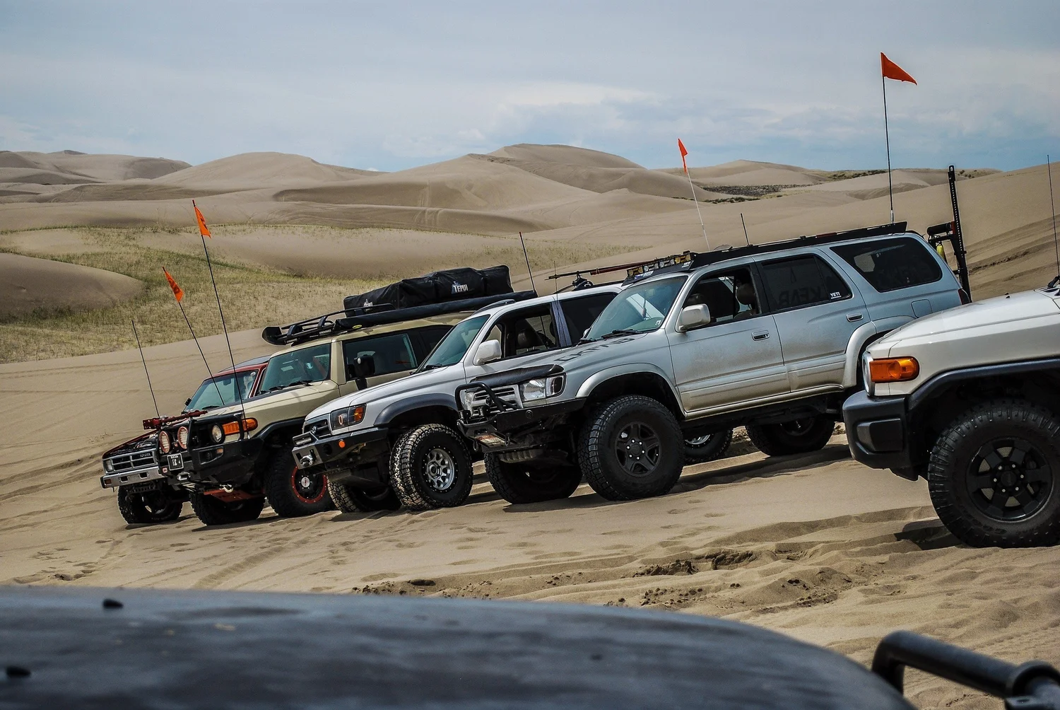 Row of flagged Toyota FJ Cruisers and 4Runners staged with dunes behind at the St. Anthony Sand Dunes in Idaho