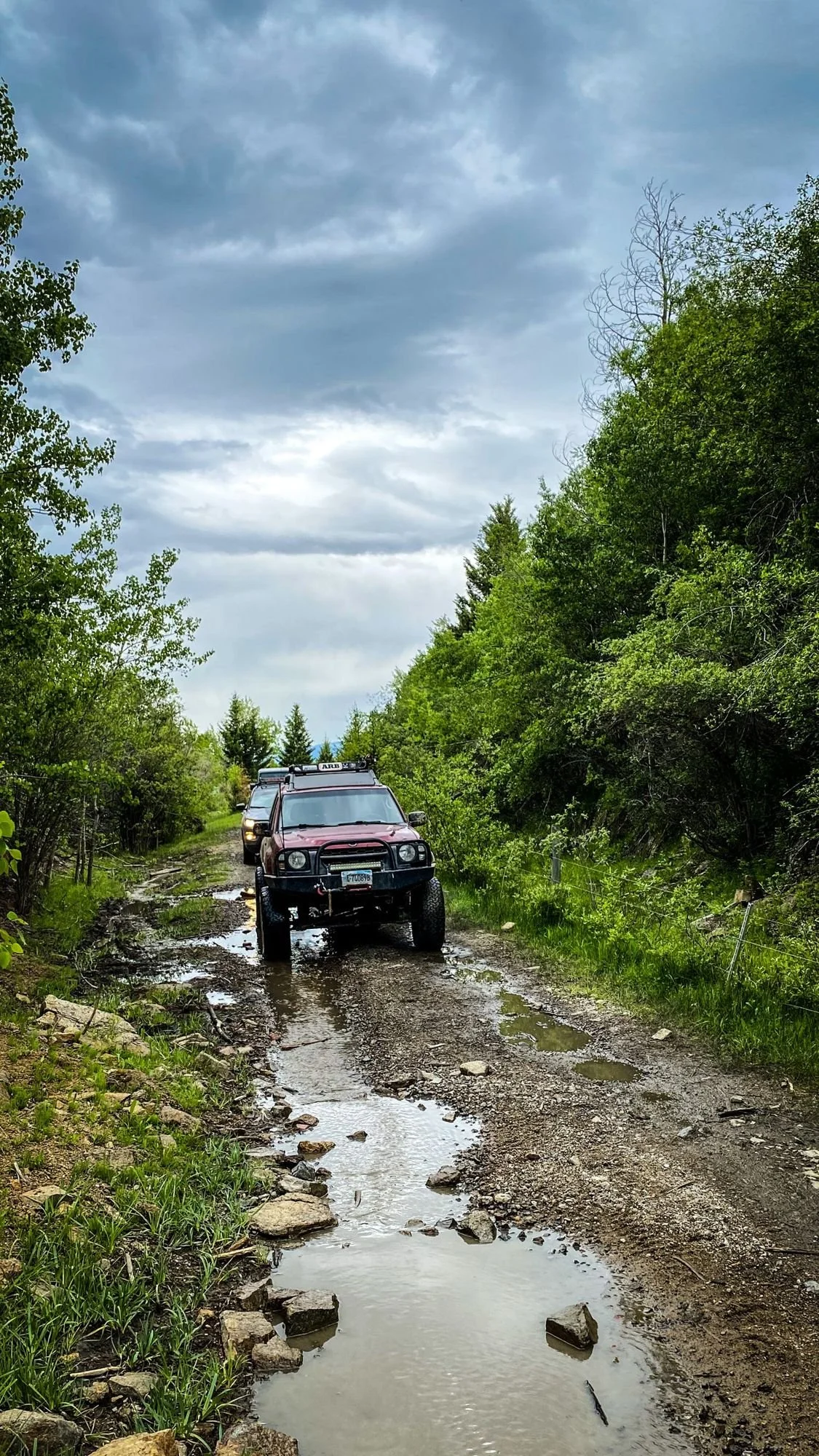 Red truck on a wet, puddled two-track climbing toward the Wickes tunnel under a cloudy sky at the Wickes railroad tunnel near Jefferson City, Montana