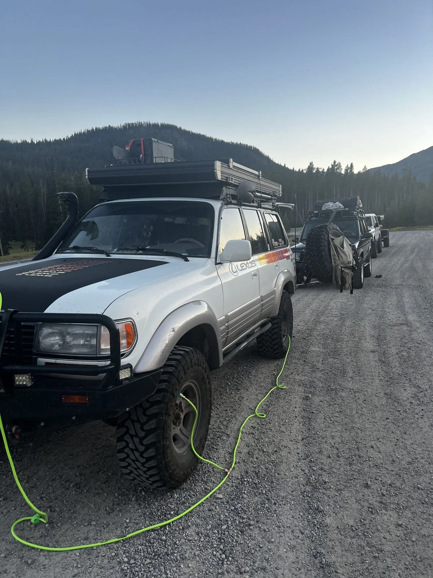 Lexus LX450 on a gravel road with a line of trucks behind near Cooke City, Montana