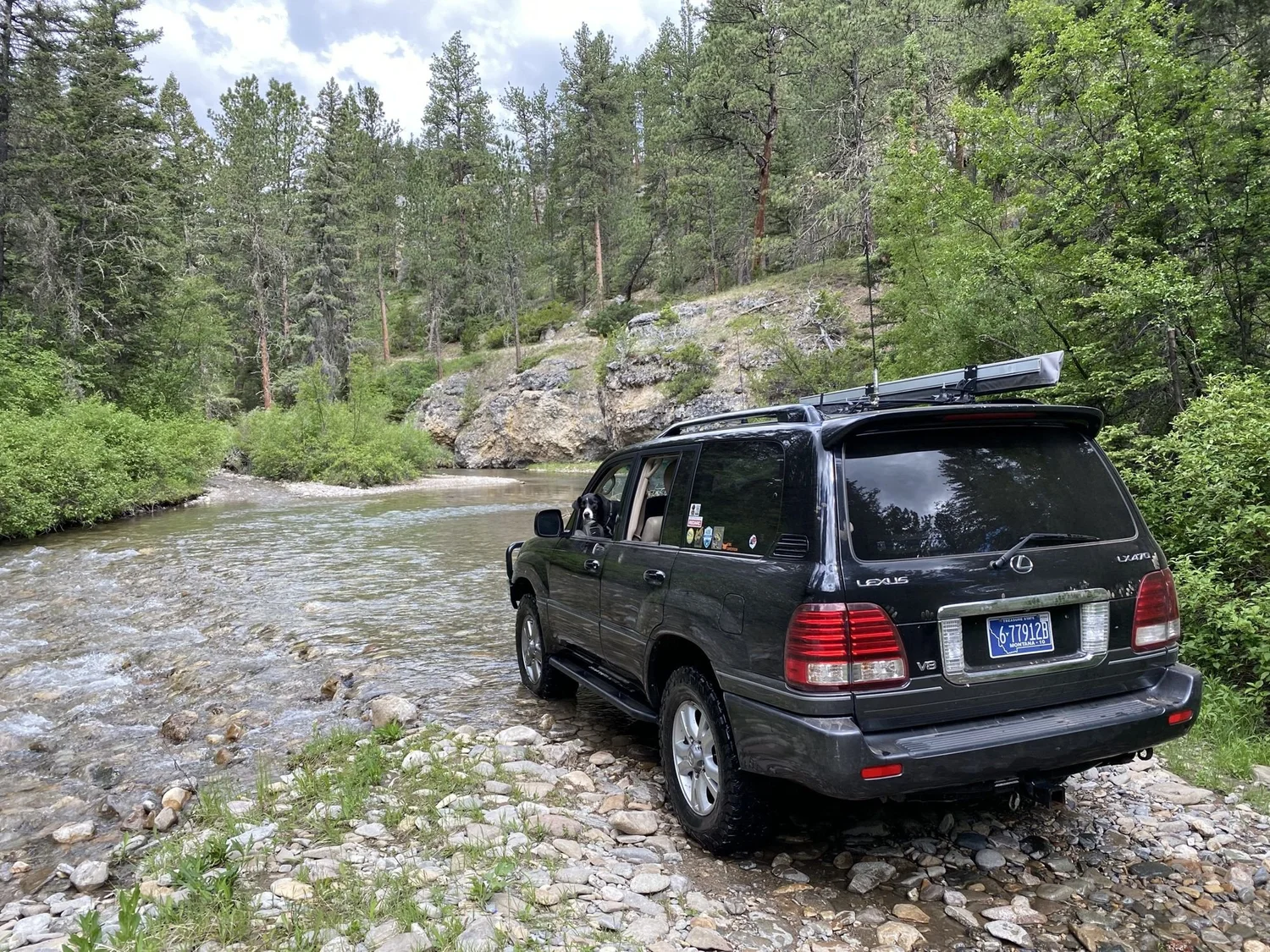 Black Lexus LX 470 climbing out of a clear creek onto a gravel bank on the Middle Fork Judith River road in the Little Belt Mountains, Montana