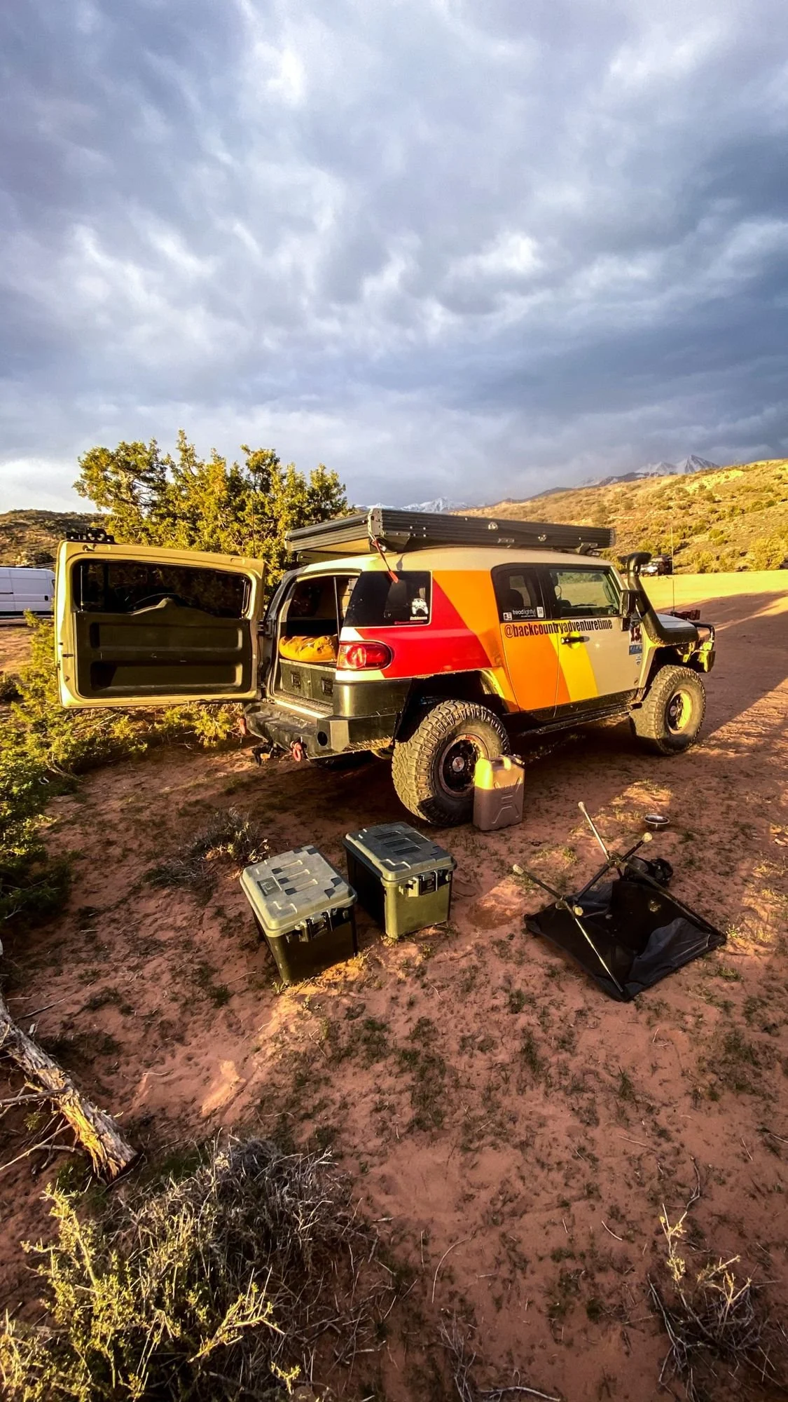Striped FJ Cruiser with doors open at a desert camp with gear on the red sand on a spring road trip through Utah