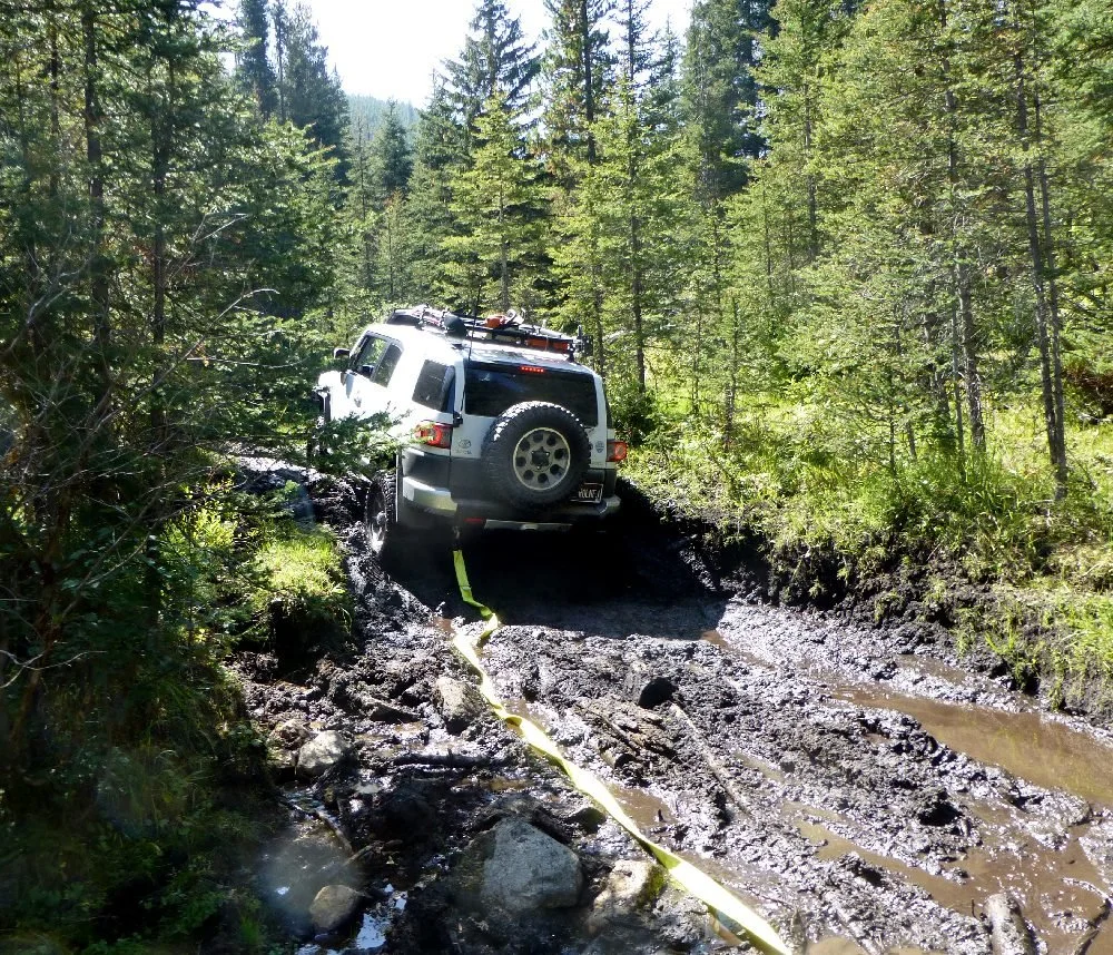 FJ Cruiser stuck in a deep mud hole with a yellow recovery strap attached