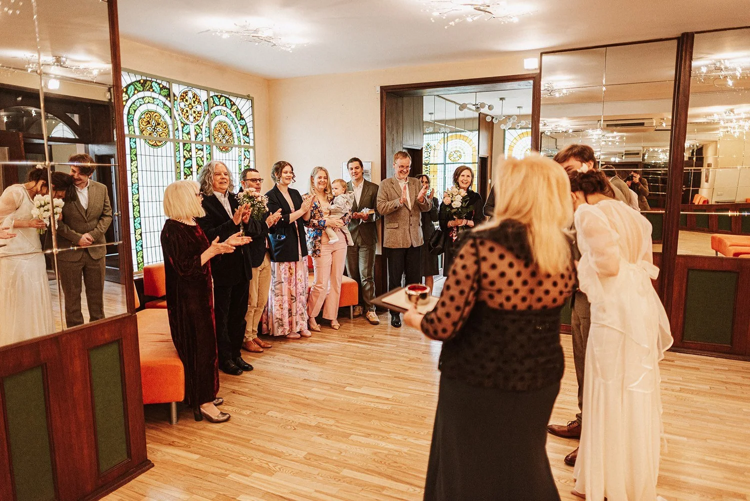 Viesi sagaida pāri ceremonijas telpā pie vitrāžas.