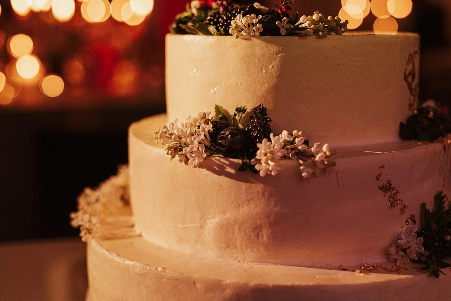 Kāzu torte ar ziediem siltā gaismiņu fonā.