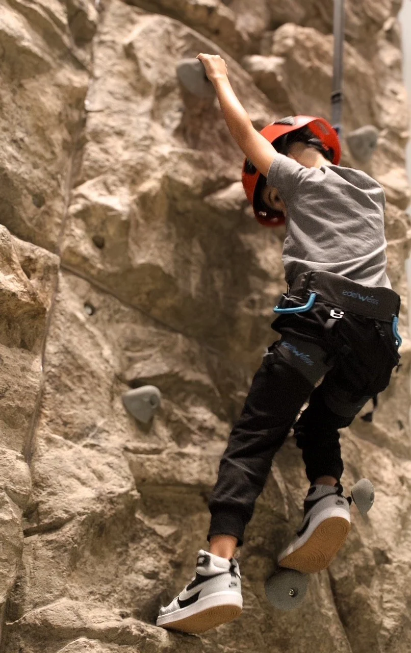 Young climber in a helmet scaling the rock wall at Silver Stone Castle in Swansea, MA