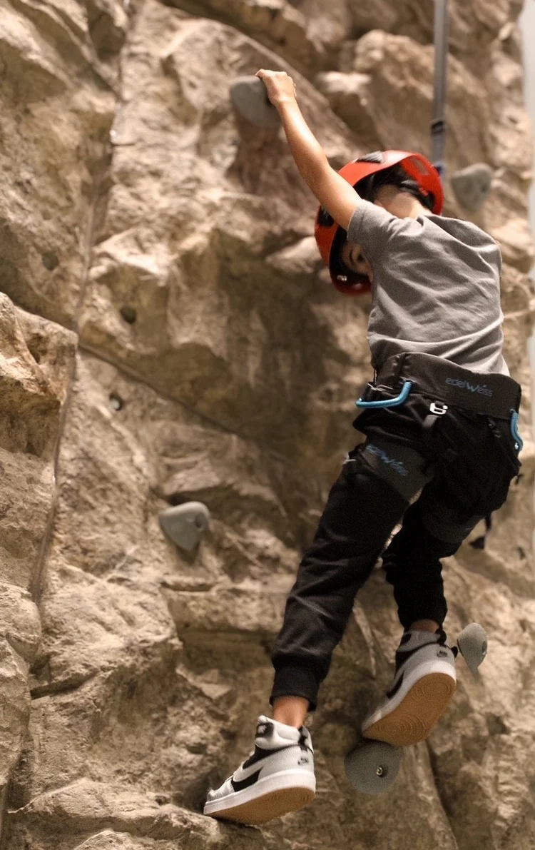 Young climber in a helmet scaling the rock wall at Silver Stone Castle in Swansea, MA