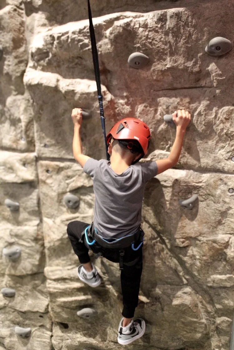 Kid in a red helmet climbing the rock wall at Silver Stone Castle, Swansea, MA