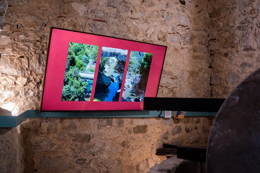 Tre fotografie verticali del fiume Bussento su uno schermo dal fondo rosso, appeso alla parete in pietra