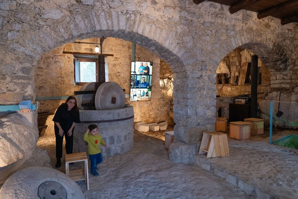 Gli archi in pietra del frantoio con la macina, uno schermo verticale e una visitatrice con un bambino