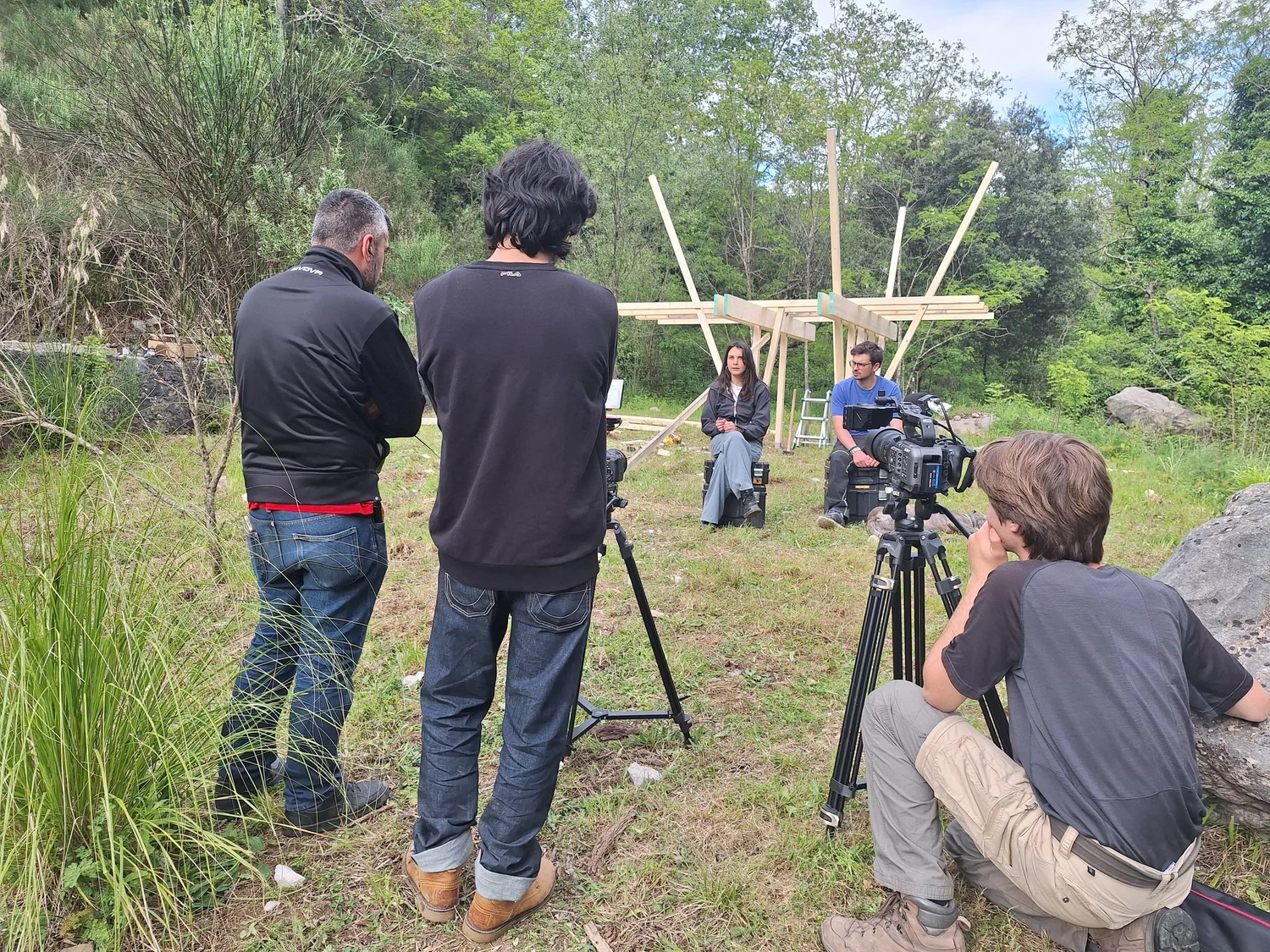 Intervista all'aperto nel verde: Daniele De Stefano di spalle con due allievi, la troupe riprende la persona intervistata