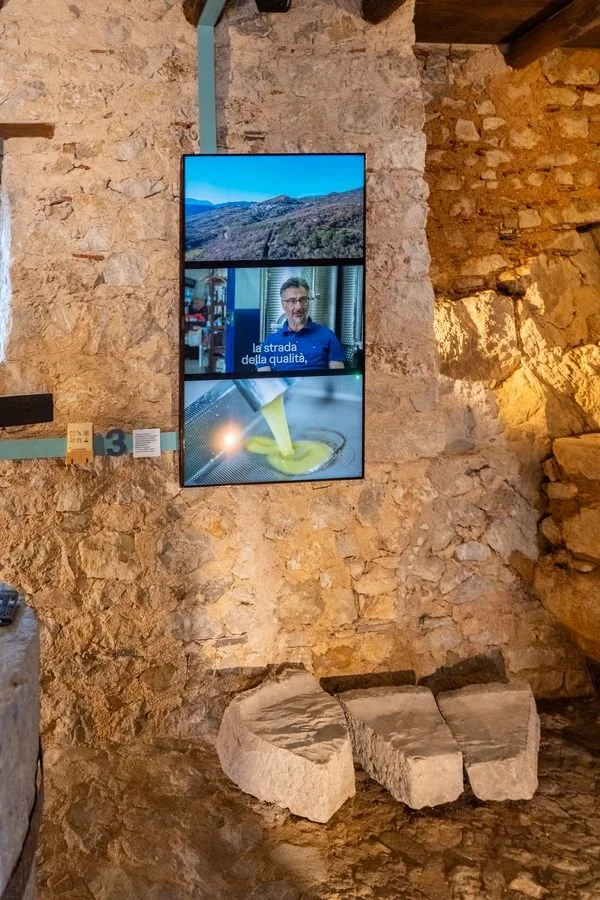 Lo schermo verticale reale appeso alla parete in pietra del frantoio, sopra frammenti di macina