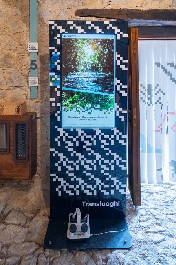 Il totem Transluoghi con lo schermo verticale accanto alla porta del frantoio, con un visore VR alla base